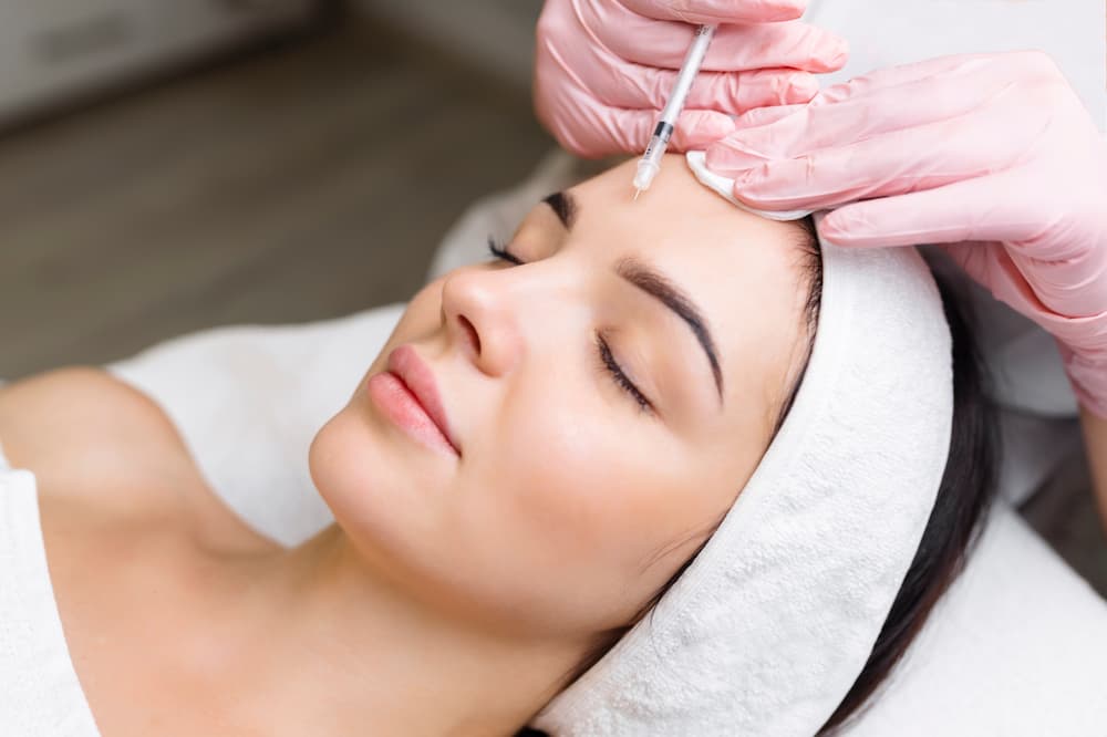 Woman receiving a forehead injection treatment, illustrating wrinkle reduction options when comparing DAXXIFY® vs BOTOX® for smoother skin.