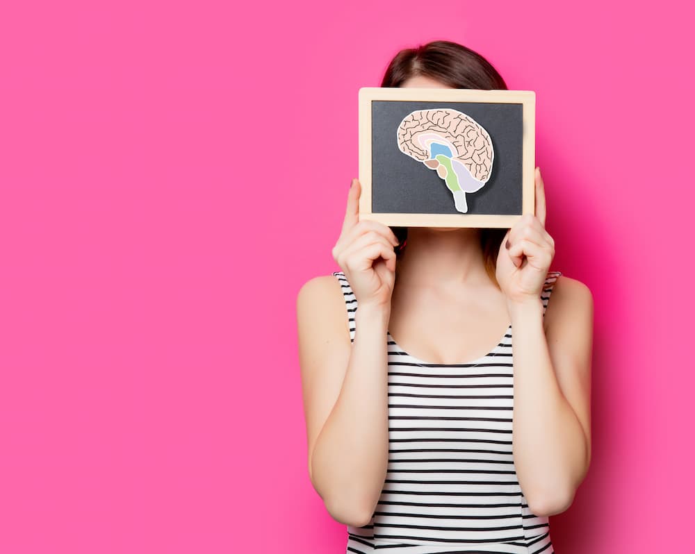Woman holding a chalkboard with a brain illustration representing how hormonal imbalance affects brain health