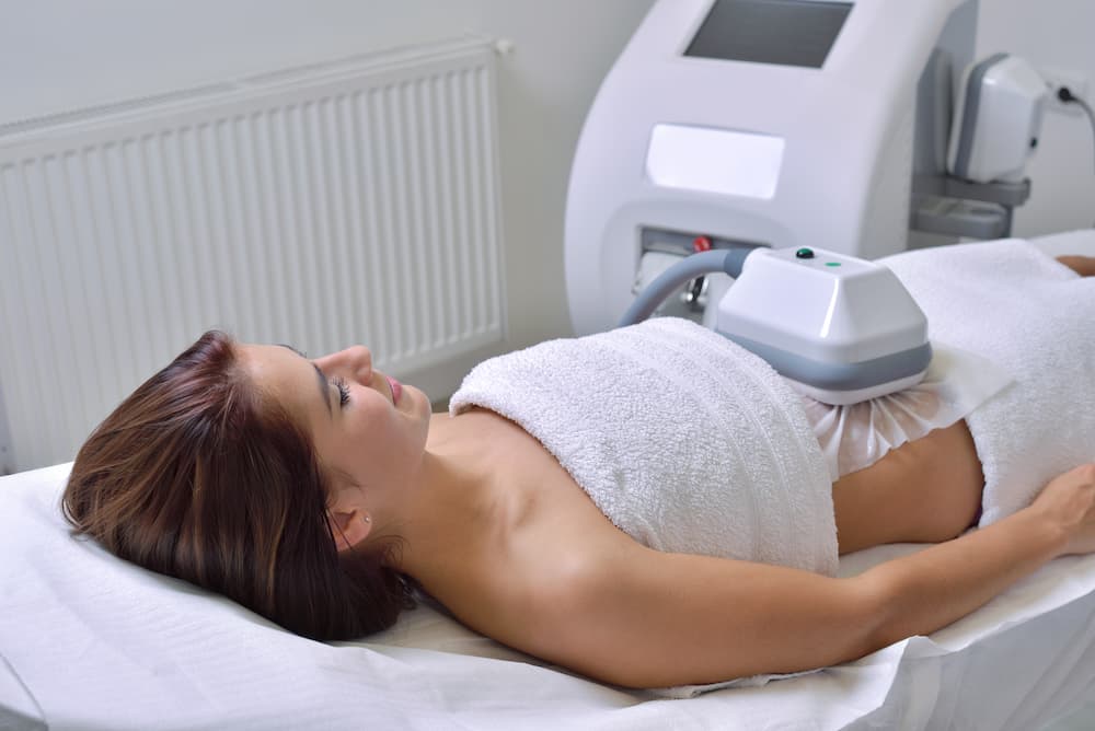 Woman receiving a CoolSculpting treatment with a cryolipolysis applicator on her abdomen at a medical aesthetics clinic