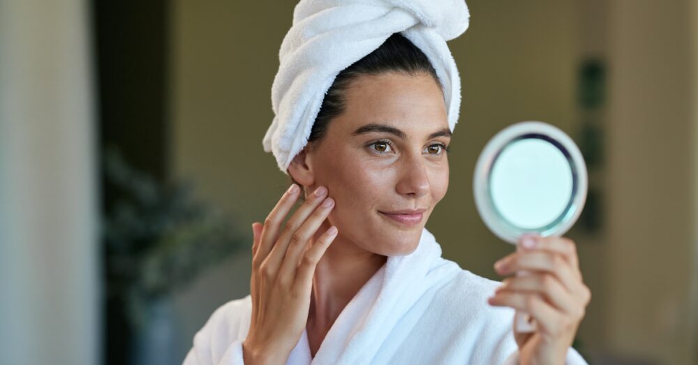 Woman in a spa robe examining her facial results in a mirror