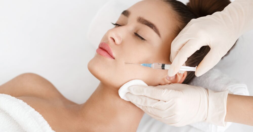 A person receiving a facial injection along the jawline from a gloved practitioner