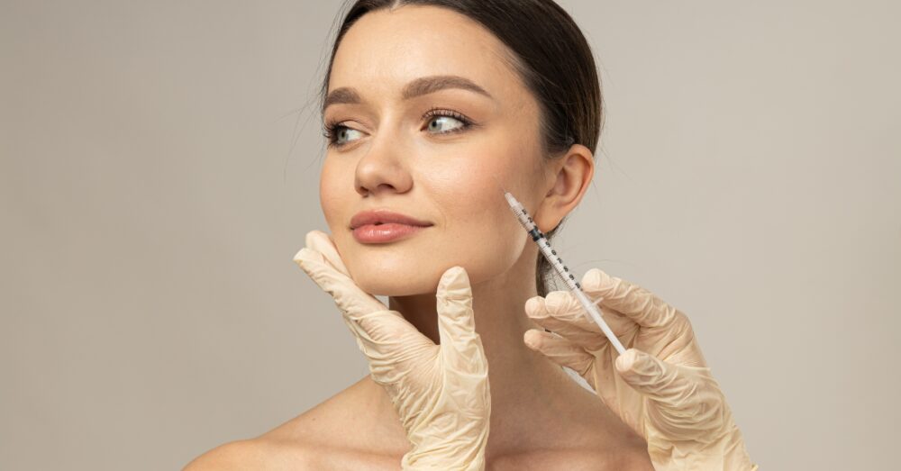 A person looking to the side while a gloved practitioner administers an injection near the lower jaw
