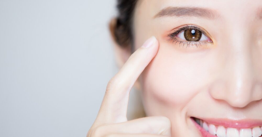 A close-up of a woman gently touching the skin beneath her eye to highlight the under eye area