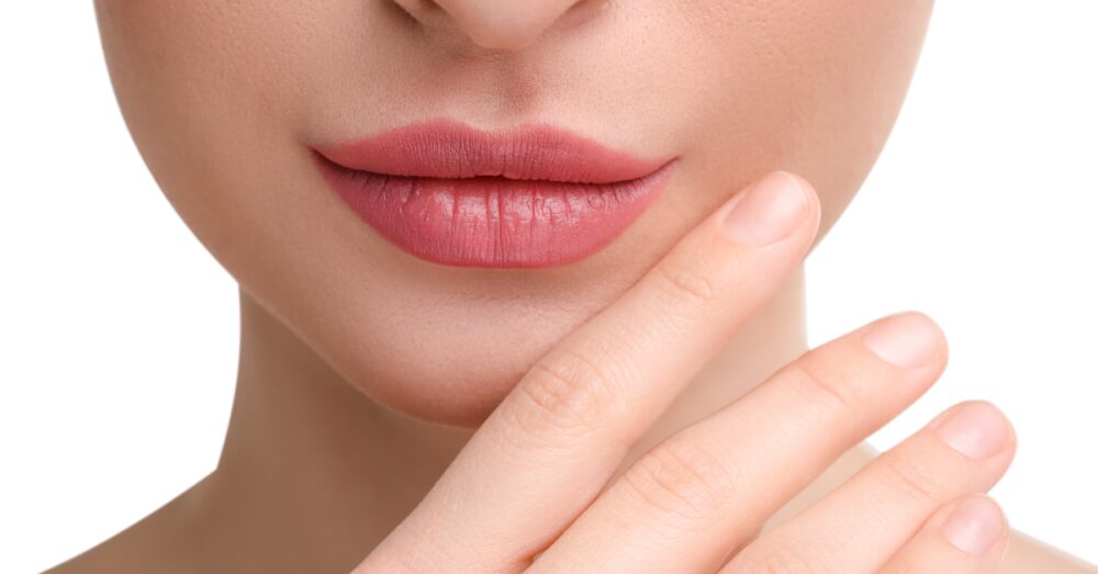 Close up of a woman with full lips lightly touching her chin against a white background