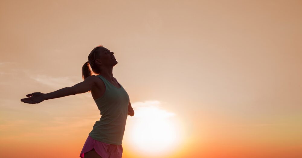 Woman standing against the sunset with her stretched out
